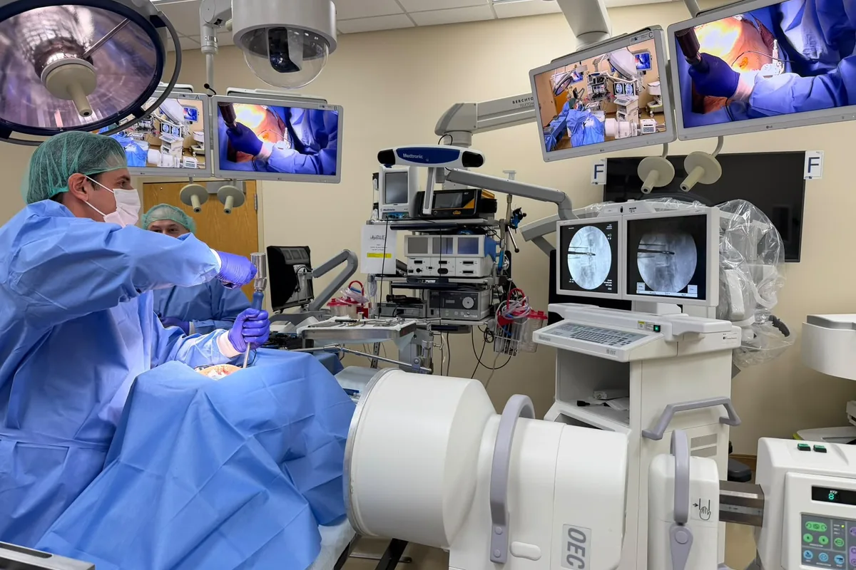 Dr. Guilherme Gontijo em sala de treinamento cirúrgico com monitores de navegação e arco de imagem para cirurgia da coluna